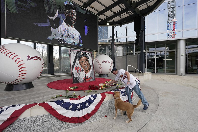 A man places flowers next to a portrait Atlanta Braves' Hank Aaron outside Truist Park, Friday, Jan. 22, 2021, in Atlanta. Aaron, who endured racist threats with stoic dignity during his pursuit of Babe Ruth but went on to break the career home run record in the pre-steroids era, died peacefully in his sleep early Friday. He was 86. (AP Photo/John Bazemore
