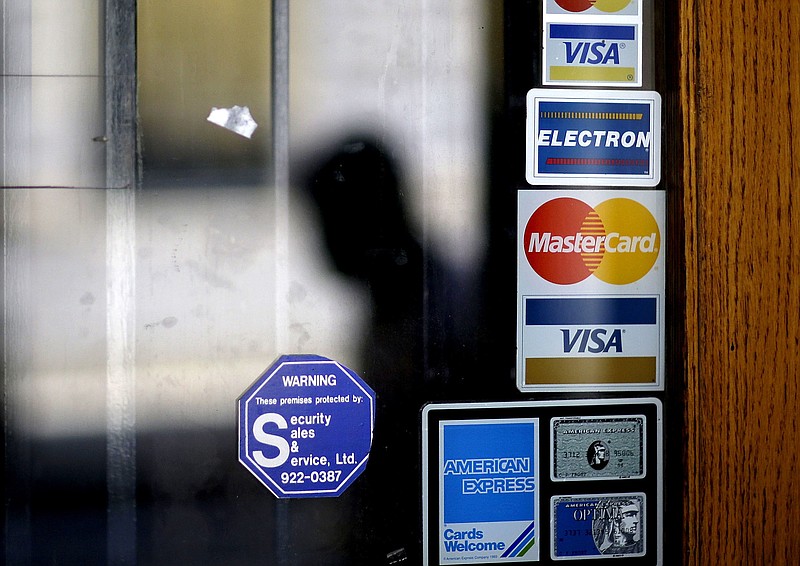 FILE - In this July 18, 2012, file photo, a pedestrian passes credit card logos posted on a downtown storefront in Atlanta. Many consumers want to pay off their debt in 2021 but are unsure how to navigate the COVID-19 economy. Experts recommend listing all your debts and contacting each lender to see if it will reduce your interest rate, lower your monthly payment or waive late fees.  (AP Photo/David Goldman, File)