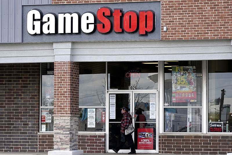 FILE - In this Oct. 15, 2020 file photo, a woman wears a face mask as she walks past a GameStop store in Des Plaines, Ill. Two hedge funds are bowing out of their short positions on the money-losing video game retailer. Citron Research’s Andrew Left said in a video posted on YouTube that his company is going to become more judicious in shorting stocks. Melvin Capital is also exiting GameStop, with manager Gabe Plotkin telling CNBC that the hedge fund was taking a significant loss.  (AP Photo/Nam Y. Huh, File)