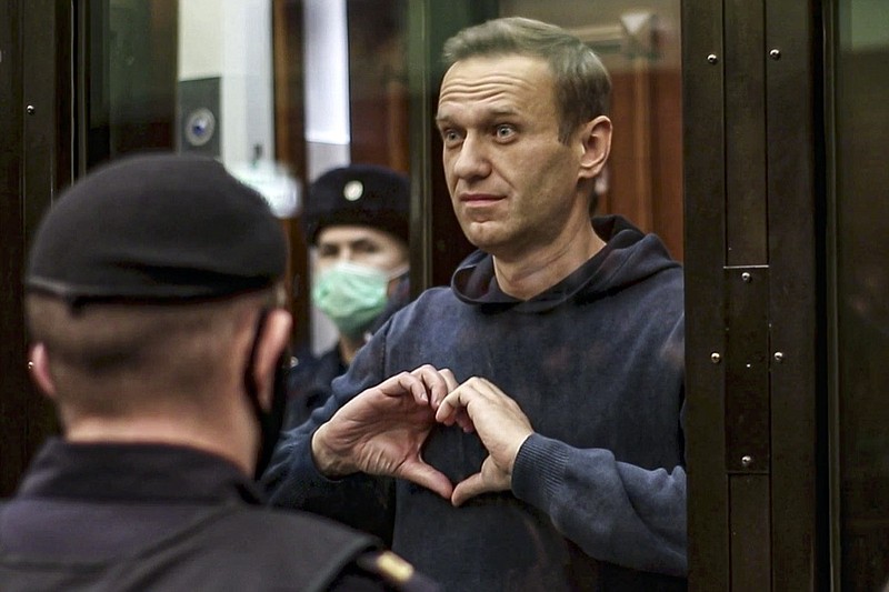 In this handout photo taken from a footage provided by Moscow City Court, Russian opposition leader Alexei Navalny shows a heard symbol standing in the cage during a hearing to a motion from the Russian prison service to convert the suspended sentence of Navalny from the 2014 criminal conviction into a real prison term in the Moscow City Court in Moscow, Russia, Tuesday, Feb. 2, 2021. A Moscow court has ordered Russian opposition leader Alexei Navalny to prison for more than 2 1/2 years for violating the terms of his probation while he was recuperating in Germany from nerve-agent poisoning. Navalny, who is the most prominent critic of President Vladimir Putin, had earlier denounced the proceedings as a vain attempt by the Kremlin to scare millions of Russians into submission. (Moscow City Court via AP)