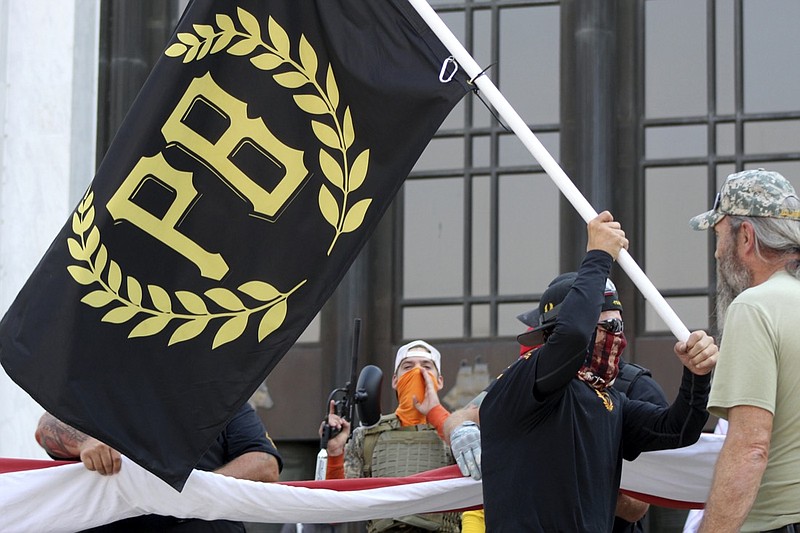 FILE - In this Sept. 7, 2020, file photo, a protester carries a Proud Boys banner, a right-wing group, while other members start to unfurl a large U.S. flag in front of the Oregon State Capitol in Salem, Ore. The Canadian government designated the Proud Boys group as a terrorist entity on Wednesday, Feb. 3, 2021, noting they played a pivotal role in the insurrection at the U.S. Capitol on Jan. 6. (AP Photo/Andrew Selsky, File)