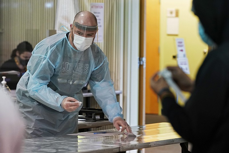 AP photo by Ted S. Warren / Pacific Lutheran football coach Brant McAdams, left, wears personal protective equipment as he prepares to give COVID-19 tests to student-athletes on Wednesday in Tacoma, Wash.