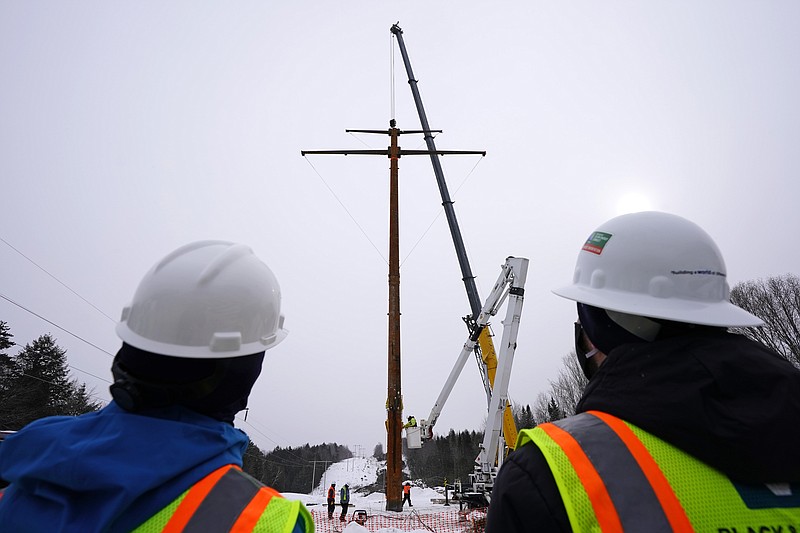 Workers watch the installation of the first pole of Central Maine Power's controversial hydropower transmission corridor, Tuesday, Feb. 9, 2021, near The Forks, Maine. The pole was erected on an existing corridor that had been widened near Moxie Pond. (AP Photo/Robert F. Bukaty)