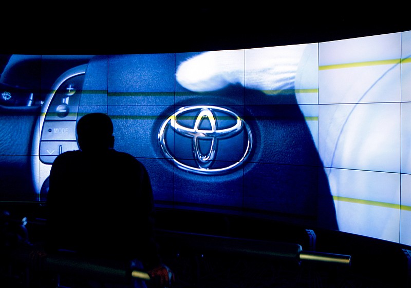 A Toyota corporate logo appears on a screen as a visitor watches a video showing the assembly line procedures of a Toyota Motor Corp.'s plant at the automaker's exhibition hall in Toyota, central Japan, Thursday, March 4, 2010. Toyota says it will roll out two new battery-electric vehicles and one plug-in gas-electric hybrid in the U.S. this year as the parade of new EVs continues. The company gave few specifics on the vehicles during a presentation Wednesday, Feb. 10, 2021 but said one electric vehicle would be an SUV.(AP Photo/Shuji Kajiyama, file)