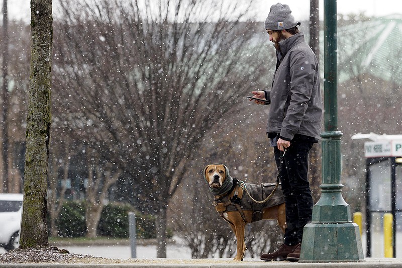 Staff photo by C.B. Schmelter / As snow falls, Andrew Walker checks his phone while waiting with his dog Hughes in Coolidge Park on Tuesday, Feb. 16, 2021 in Chattanooga, Tenn. Walker said he was just going about his morning routine.
