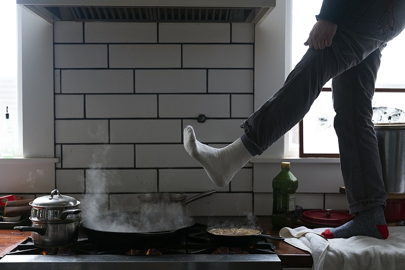 AP Photo by Ashley Landis/Jorge Sanhueza-Lyon stands on his kitchen counter to warm his feet over his gas stove Tuesday in Austin, Texas.