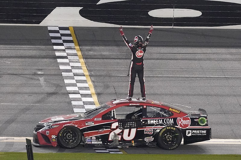 AP photo by John Raoux / Joe Gibbs Racing driver Christopher Bell stands on his car and celebrates in front of the grandstands at Daytona International Speedway after winning Sunday's NASCAR Cup Series on the road course.