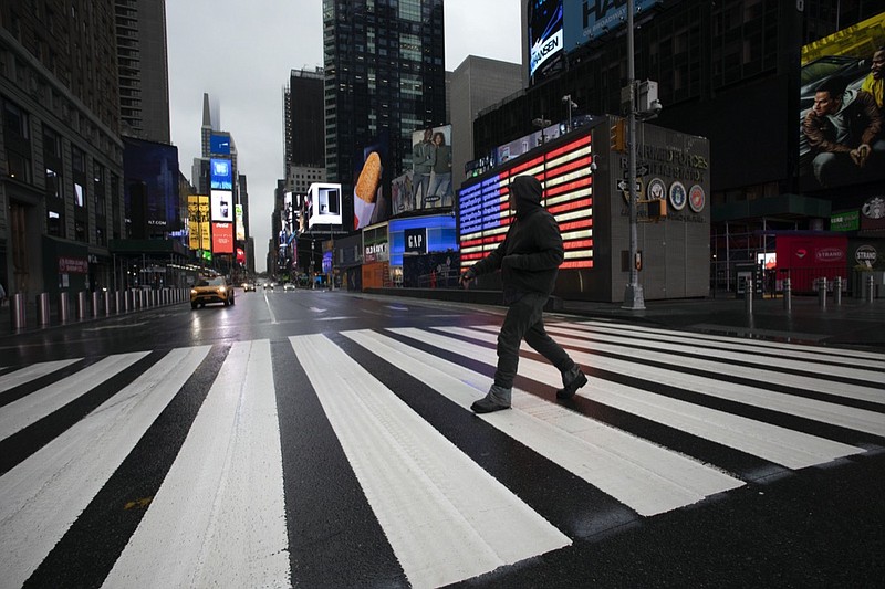 A man crosses the street in a nearly empty Times Square, which is usually very crowded on a weekday morning in New York, March 23, 2020. (AP Photo/Mark Lennihan)