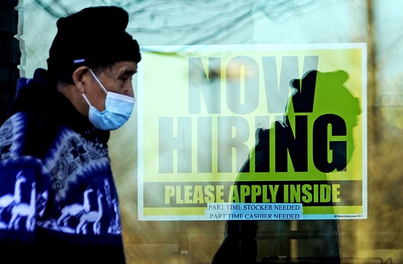 In this Nov. 28, 2020 file photo, a shopper wears a face mask and he walks past a store displaying a hiring sign in Wheeling, Ill. The number of Americans seeking unemployment benefits fell sharply last week but remained high by historical standards. Applications for benefits declined 111,000 from the previous week to a seasonally adjusted 730,000, the Labor Department said Thursday, Feb. 25. It is the lowest figure since late November. (AP Photo/Nam Y. Huh, File)