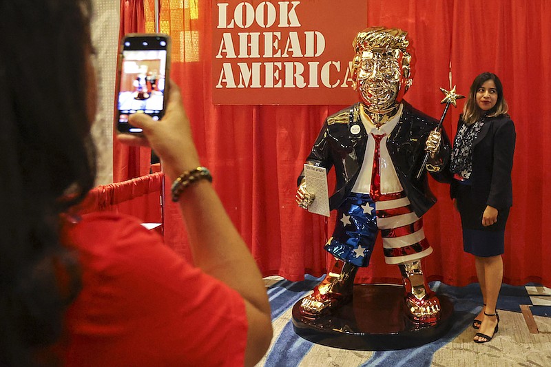 A woman takes a photo with a golden Donald Trump statue at the Conservative Political Action (CPAC) conference on Friday, Feb. 26, 2021, in Orlando, Fla. (Sam Thomas/Orlando Sentinel via AP)