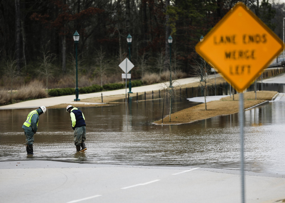 Staff photo by Troy Stolt / Construction workers Tony Platt and Jamie Mills, of Augusta, Georgia, wash red clay off of their boots in flood water on Camp Jordan Parkway on Tuesday, Feb. 11, 2020 in East Ridge, Tenn.