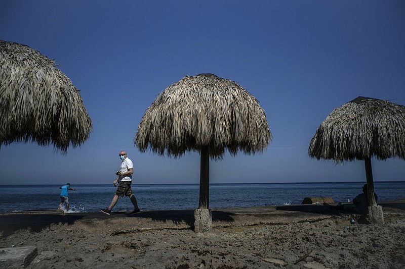 A tourist, wearing a protective face mask amid the new cornavirus pandemic, walks along the beach shore in Havana, Cuba, Tuesday, March 2, 2021. The Caribbean is hunting for visitors to jump-start the stalled economy in one of the world's most tourism-dependent regions (AP Photo/Ramon Espinosa)