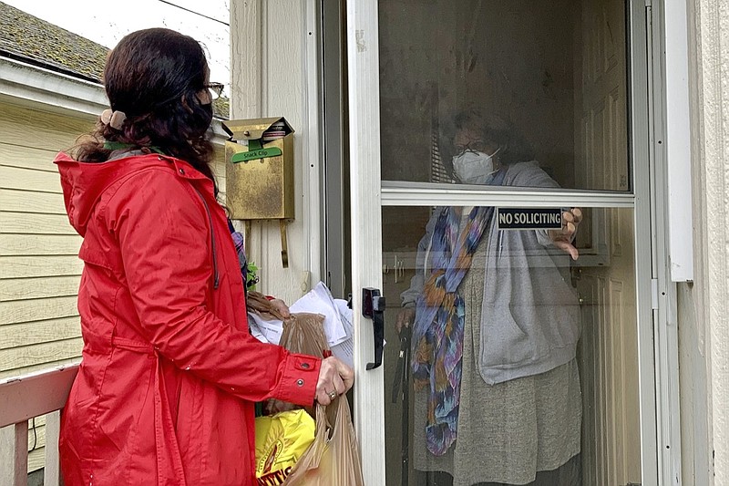 Senior citizen Barbara Bender answers the door for Store to Door employee Nancy Murphy in Portland, Ore., as she delivers an order of groceries for the nonprofit on Feb. 25, 2021. An untold number of older people are getting left behind in the desperate dash for shots because they are too frail, overwhelmed, isolated or poor to navigate a system that favors healthier individuals with more resources. Nonprofits, churches and health care outreach workers are scrambling to to reach older people who are falling through the cracks before the nation's focus moves on and the competition for vaccines stiffens. (AP Photo/Gillian Flaccus)

