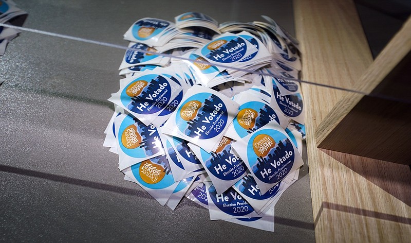 FILE - In this Oct. 30, 2020, file photo stickers printed in Spanish sit on the desk of an election judge to be distributed to voters after they cast their ballots in the atrium of Ball Arena, the home of the NBA's Denver Nuggets and the NHL's Colorado Avalanche in Denver. (AP Photo/David Zalubowski, File)

