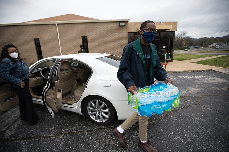 Staff photo by Troy Stolt / Samuel Brand, right, carries a case of water bottles Princess Brooks, left, donated to Orchard Park SDA church during a water bottle drive to help residents of Jackson, Mississippi, who have been without water for nearly a month, after freezing temperatures burst water mains in February on Saturday, March 13, 2021 in Chattanooga, Tenn.