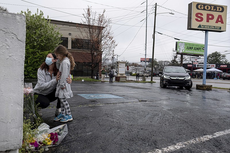 Mallory Rahman and her daughter Zara Rahman, 4, who live nearby, pause after bringing flowers to the Gold Spa massage parlor in Atlanta, Wednesday afternoon, March 17, 2021, the day after eight people were killed at three massage spas in the Atlanta area. Authorities have arrested 21-year-old Robert Aaron Long in the shootings at massage parlors in Atlanta and one in Cherokee County. (AP Photo/Ben Gray)