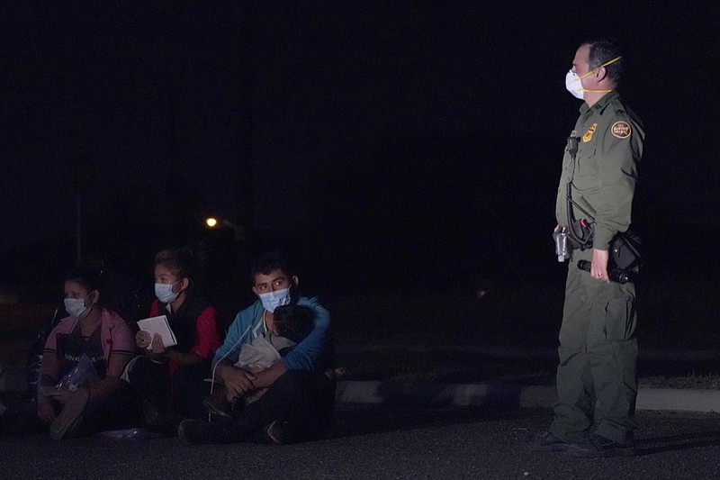 A migrant man, center, holds a child as he looks at a U.S. Customs and Border Protection agent at an intake area after crossing the U.S.-Mexico border, early Wednesday, March 24, 2021, in Roma, Texas. A surge of migrants on the Southwest border has the Biden administration on the defensive. The head of Homeland Security acknowledged the severity of the problem but insisted it's under control and said he won't revive a Trump-era practice of immediately expelling teens and children. (AP Photo/Julio Cortez)