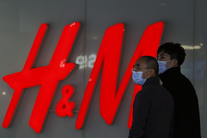 Visitors to a shopping mall wearing masks pass by an H&M store in Beijing on Monday, March 29, 2021. China stepped up pressure Monday on foreign shoe and clothing brands to reject reports of abuses in Xinjiang, telling companies that are targeted by Beijing for boycotts to look more closely and pointing to a statement by one that it found no forced labor. (AP Photo/Ng Han Guan)