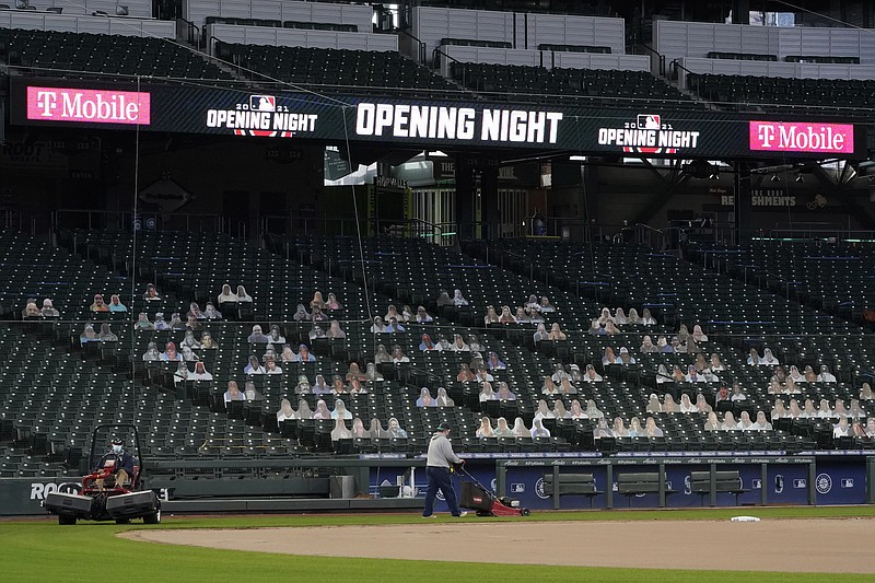 Grounds crew workers mow near the first-base foul line at T-Mobile Park, the home of the Seattle Mariners baseball team, Monday, March 22, 2021, in Seattle as photos in the stands demonstrate how fans attending reduced-capacity games will be separated into "seating pods" to avoid the spread of COVID-19. The Mariners are scheduled host the San Francisco Giants on April 1 in the Mariners' home-opener. (AP Photo/Ted S. Warren)