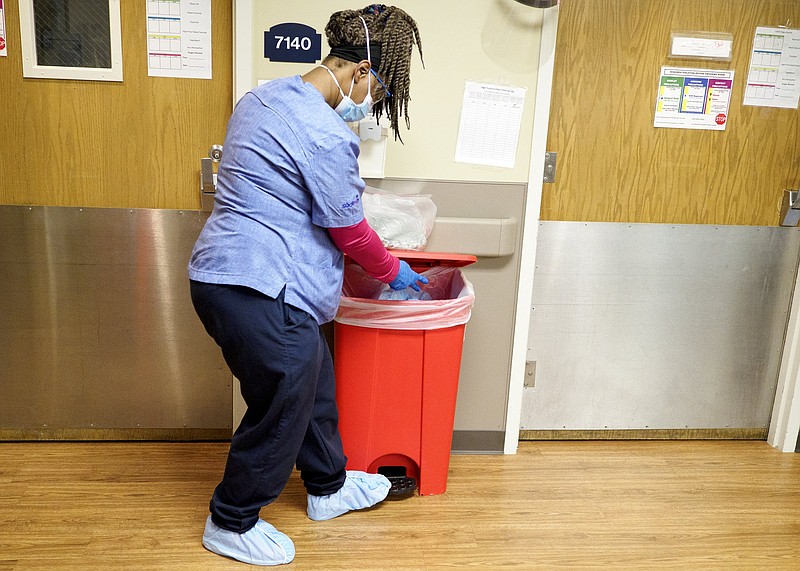 Staff photo by C.B. Schmelter / Housekeeper Towanda Marshall demonstrates how she disposes of her personal protective equipment after cleaning a room on the COVID floor at Erlanger on Monday, Feb. 22, 2021, in Chattanooga, Tenn.