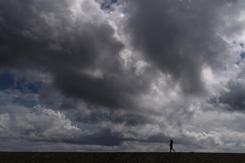In this March 10, 2021, file photo, a woman strolls along the beach under rain clouds in Seal Beach, Calif. Rainstorms grew more erratic and droughts much longer across most of the U.S. West over the past half-century as climate change warmed the planet, according to a sweeping government study released, Tuesday, April 6, 2021, that concludes the situation in the region is worsening. (AP Photo/Jae C. Hong, File)
