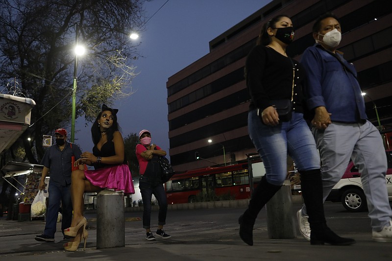 Sex worker Geraldine wearing cat make-up sits on her usual corner as she waits for clients outside the Revolution subway station, in Mexico City, Saturday, March 13, 2021. Geraldine, 30, a sex worker since age 15, says many of her regular clients have stopped coming amid the coronavirus pandemic and that seeing new clients presents new health and security risks. She is most concerned about the risk of bringing COVID-19 home to her partner, who has diabetes. (AP Photo/Rebecca Blackwell)