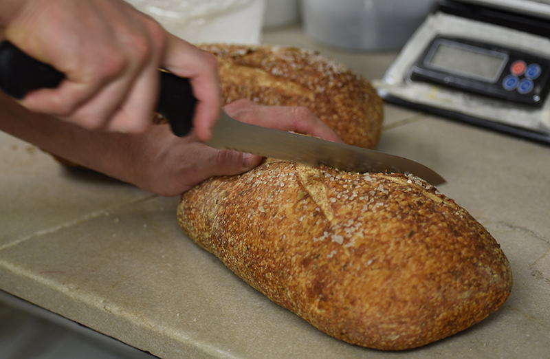 Staff photo by Matt Hamilton / Dane Frazier slices into a loaf of his rosemary sourdough.