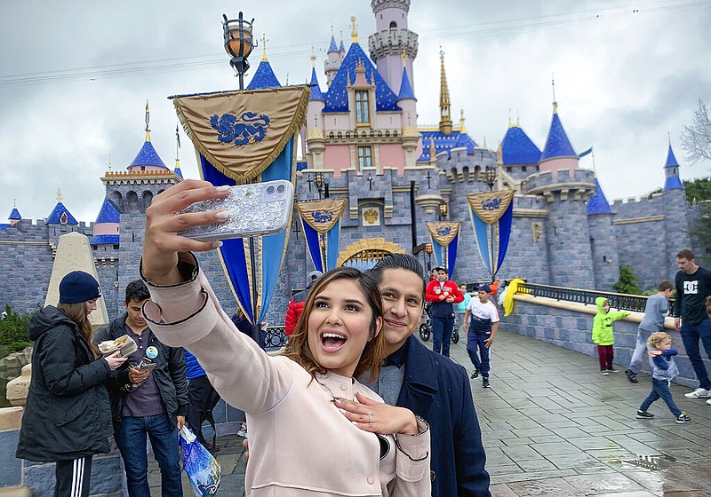 In this March 13, 2020, file photo, Katherine Quezada shows off her engagement ring as she takes a selfie with her new fiance, Fernando Carranza, in front of Sleeping Beauty Castle the during the last day before Disneyland closes because of the COVID-19 coronavirus outbreak, in Anaheim, Calif. Carranza proposed to Quezada in front of the castle earlier that day. Disneyland Park and Disney California Adventure park will reopen to visitors on Friday, April 30, 2021. (Jeff Gritchen/The Orange County Register via AP, File)