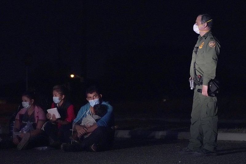 In this March 24, 2021 photo, a migrant man, center, holds a child as he looks at a U.S. Customs and Border Protection agent at an intake area after crossing the U.S.-Mexico border, early Wednesday, March 24, 2021, in Roma, Texas. The Biden administration said Monday that four families that were separated at the Mexico border during Donald Trump's presidency will be reunited in the United States this week in what Homeland Security Secretary Alejandro Mayorkas calls "just the beginning" of a broader effort. (AP Photo/Julio Cortez)