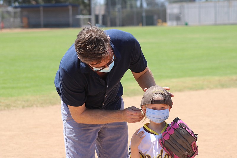 Dr. Kit Nazor, a Chattanooga native, helps daughter Charleana put her face mask back on as she returns to the dugout during a T-ball game in San Diego.