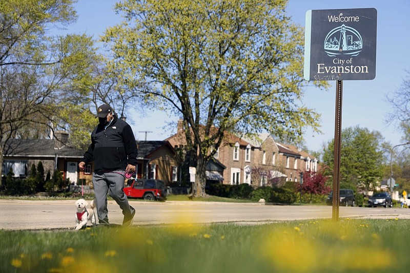 A person walks a dog past a street sign reading "Welcome to Evanston" in the predominantly Black 5th Ward in Evanston, Ill., Tuesday, May 4, 2021. The Chicago suburb is preparing to pay reparations in the form of housing grants to Black residents who experienced housing discrimination. (AP Photo/Shafkat Anowar)
