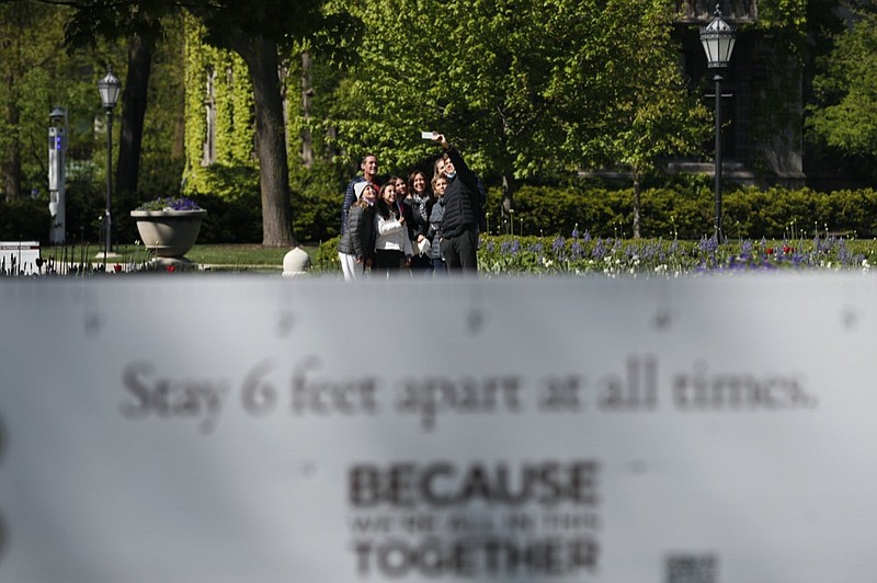 A group of visitors take a selfie near a sign reading "stay 6 feet apart at all times," Thursday, May 6, 2021, on the University of Chicago campus in Chicago. (AP Photo/Shafkat Anowar)


