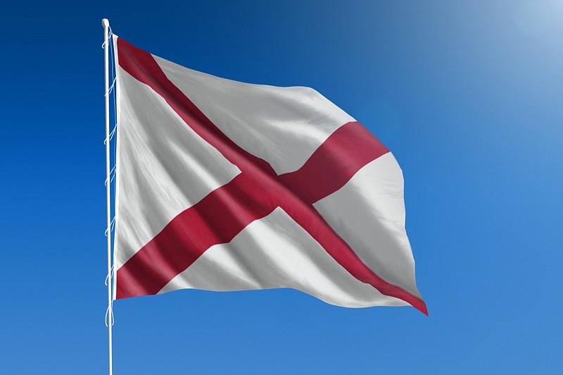 The flag of the state of Alabama blowing in the wind in front of a clear blue sky alabama flag tile / Getty Images
