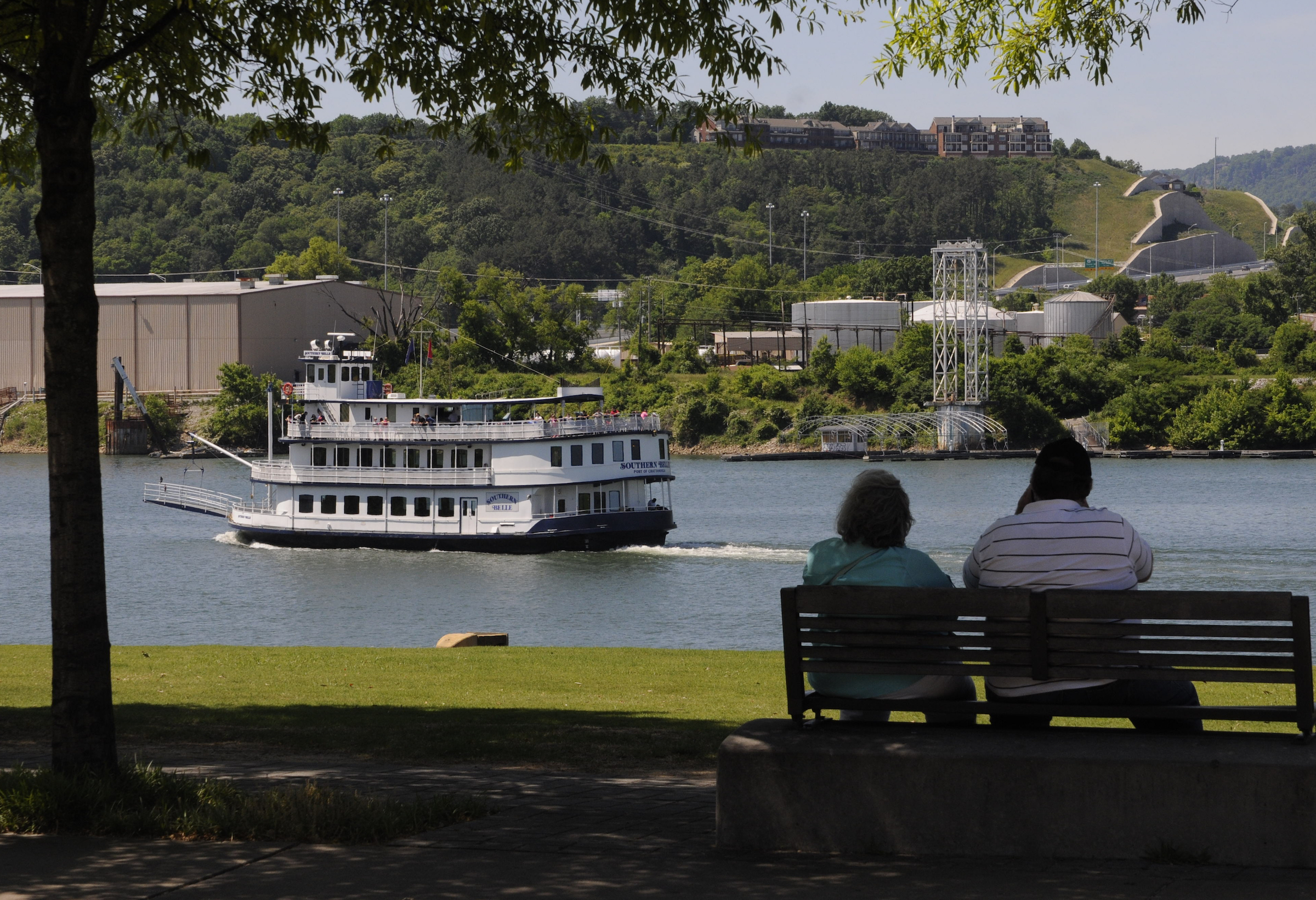 Robert and Susan Juengel, of Fayetteville, Tenn., sit in the cool shade at Ross's Landing as the Southern Belle riverboat passes with patrons atop the lookout deck.