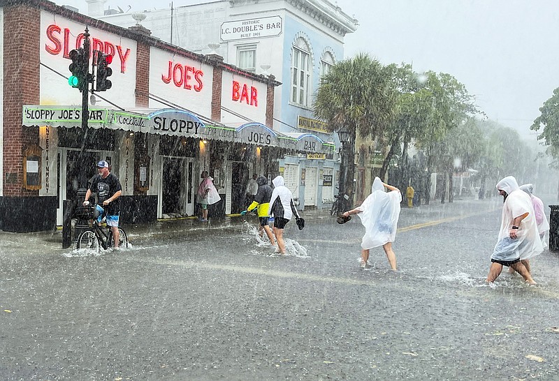 Determined visitors head for Sloppy Joe's Bar while crossing a flooded Duval Street as heavy winds and rain pass over Key West, Fla., Tuesday, July 6, 2021. The weather was getting worse in southern Florida on Tuesday morning as Tropical Storm Elsa began lashing the Florida Keys, complicating the search for survivors in the condo collapse and prompting a hurricane watch for the peninsula's upper Gulf Coast. (Rob O'Neal/The Key West Citizen via AP)