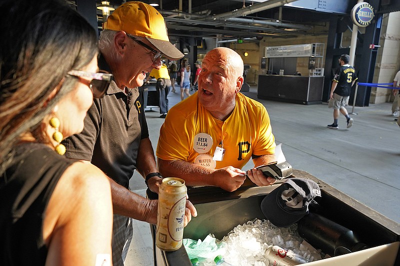 Tom Congdon, center, a vendor at Pittsburgh sports venues for 38 years, mans his beer and water cart in the concourse at PNC Park for a baseball game between the Pittsburgh Pirates and the Atlanta Braves in Pittsburgh, Monday, July 5, 2021. With fans back in the stands and concessions being sold, ballpark employees have had a chance to return after the pandemic hit many of them hard. (AP Photo/Gene J. Puskar)