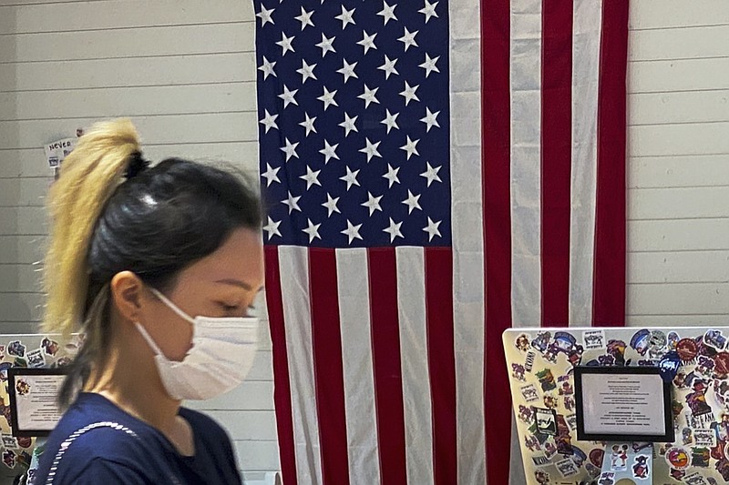 A woman wearing a face mask walks by a counter displaying an American flag at a fashion boutique in Beijing, Sunday, July 11, 2021. China on Sunday said it will take "necessary measures" to respond to the U.S. blacklisting of Chinese companies over their alleged role in abuses of Uyghur people and other Muslim ethnic minorities. (AP Photo/Andy Wong)