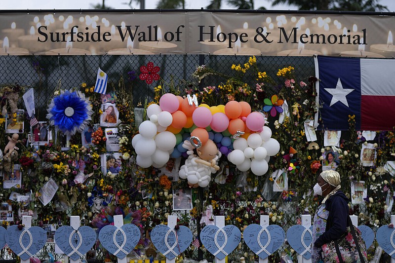 A woman walks past a makeshift memorial for the victims of the Champlain Towers South building collapse, on Monday, July 12, 2021, in Surfside, Fla.(AP Photo/Rebecca Blackwell)