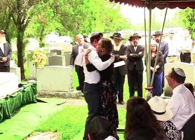 A screen capture from a livestream shows Josh Spiegel, left, hugging his sister, Rachel Spiegel, following an emotional speech during the funeral for his mother, Judy Spiegel, on Tuesday, July 13.