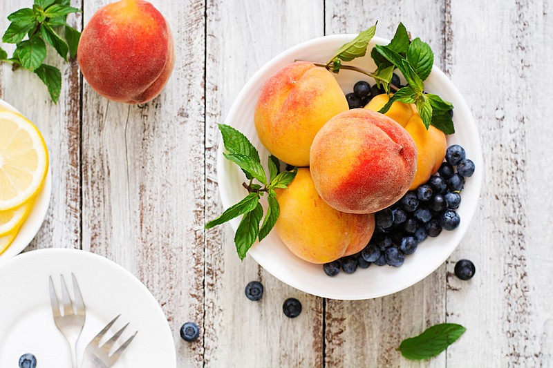 Fresh peaches and blueberries in bowl on a light wooden background in rustic style. / Photo credit: 