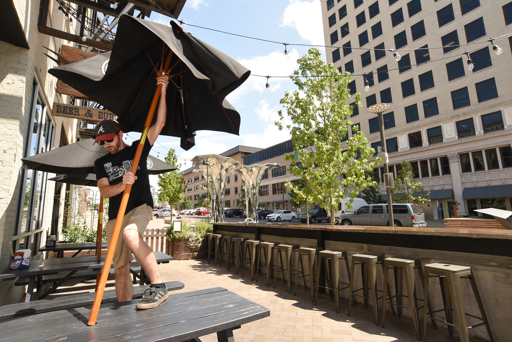 Staff Photo by Matt Hamilton / Bartender Justin Grasham puts up an umbrella in the patio area of Jack Brown's Beer & Burger Joint in the newly-renovated Patten Square on Wednesday, July 21, 2021. The eatery added the patio area when the renovations to Patten Square were completed.
