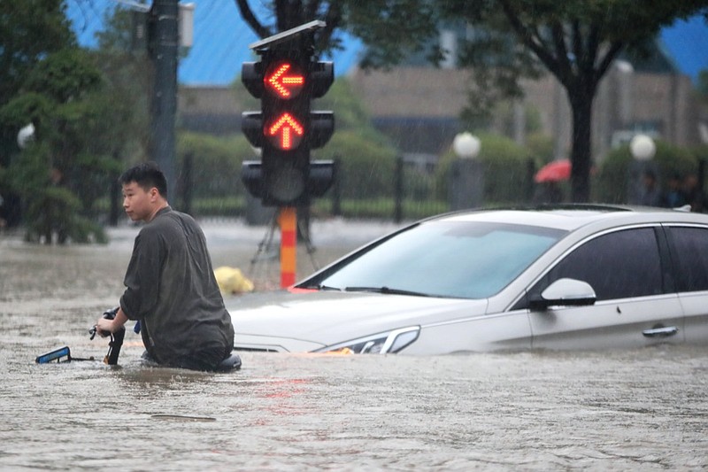 A man rides a bicycle through a flooded intersection in Zhengzhou in central China's Henan Province, Tuesday, July 20, 2021. China's military has blasted a dam to release floodwaters threatening one of its most heavily populated provinces. The operation late Tuesday night in the city of Luoyang came after several people died in severe flooding in the Henan provincial capital of Zhengzhou, where residents were trapped in the subway system and left stranded at schools, apartments and offices. (Chinatopix via AP)