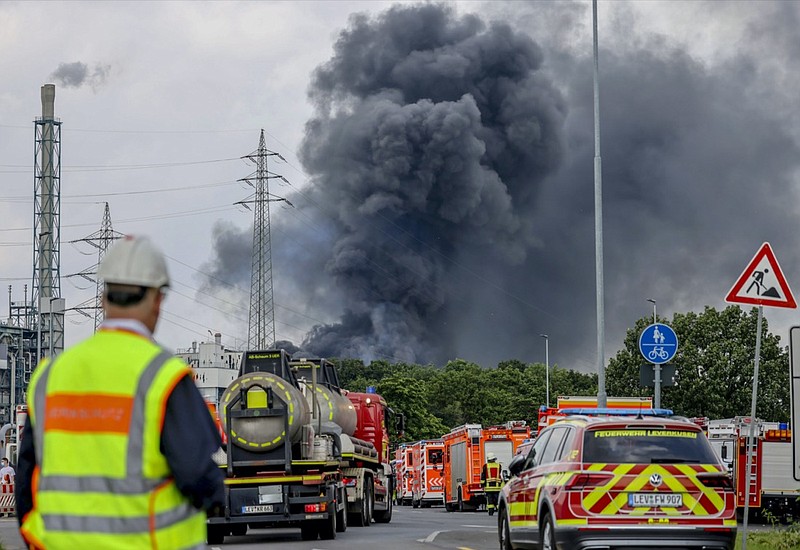 Emergency vehicles of the fire brigade, rescue services and police stand not far from an access road to the Chempark over which a dark cloud of smoke is rising in Leverkusen, Germany, Tuesday, July 27, 2021.. After an explosion, fire brigade, rescue services and police are currently in large-scale operation, the police explained. (Oliver Berg/dpa via AP)