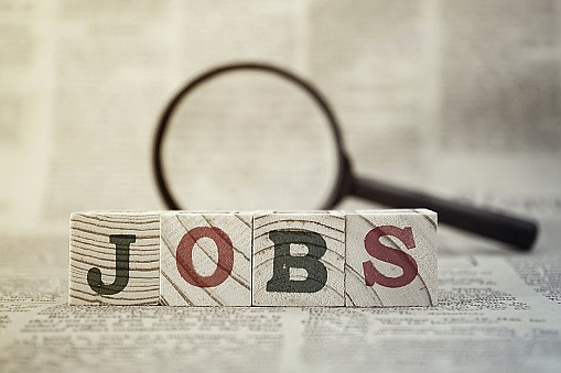 "Jobs" on wooden block and magnifying glass on newspaper background. / Getty Images/iStock