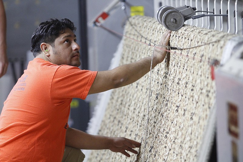 Staff file photo / Dixie Group employee Daniel Guzman, a tufting fixer, keeps an eye on new carpet and looks for any imperfections in the weave.