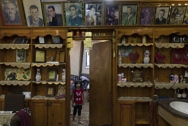 A Palestinian girl stands under framed portraits of family members, some of them were killed by the Israeli army according to Bahjat al-Alami, the grandfather of slain Mohammed al-Alami, 12, at the family house, in the West Bank village of Beit Ummar, near Hebron, Wednesday, Aug. 4, 2021. (AP Photo/Nasser Nasser)

