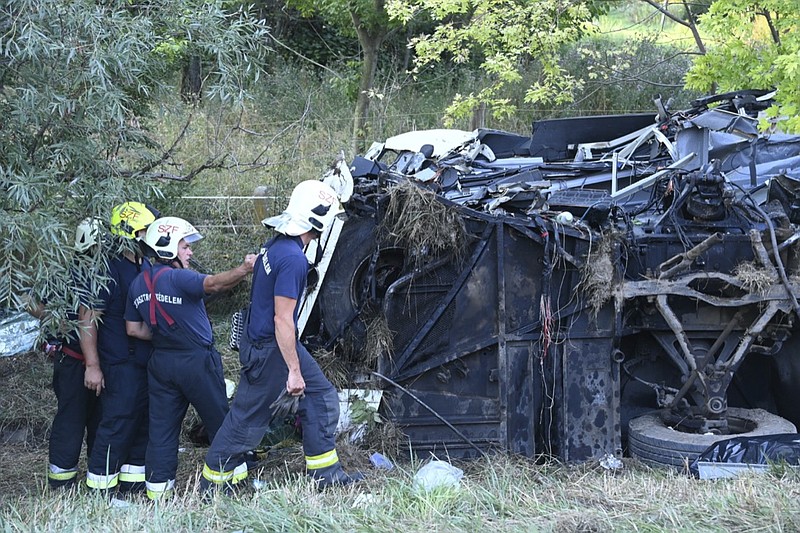 Firefighters attend the scene of a damaged bus near Szabadbattyan, Hungary, Sunday, Aug. 15, 2021, after crashing through a guardrail and tipping into a roadside ditch. Police say at least eight people are dead and dozens injured. (Zoltan Mihadak/MTI via AP)