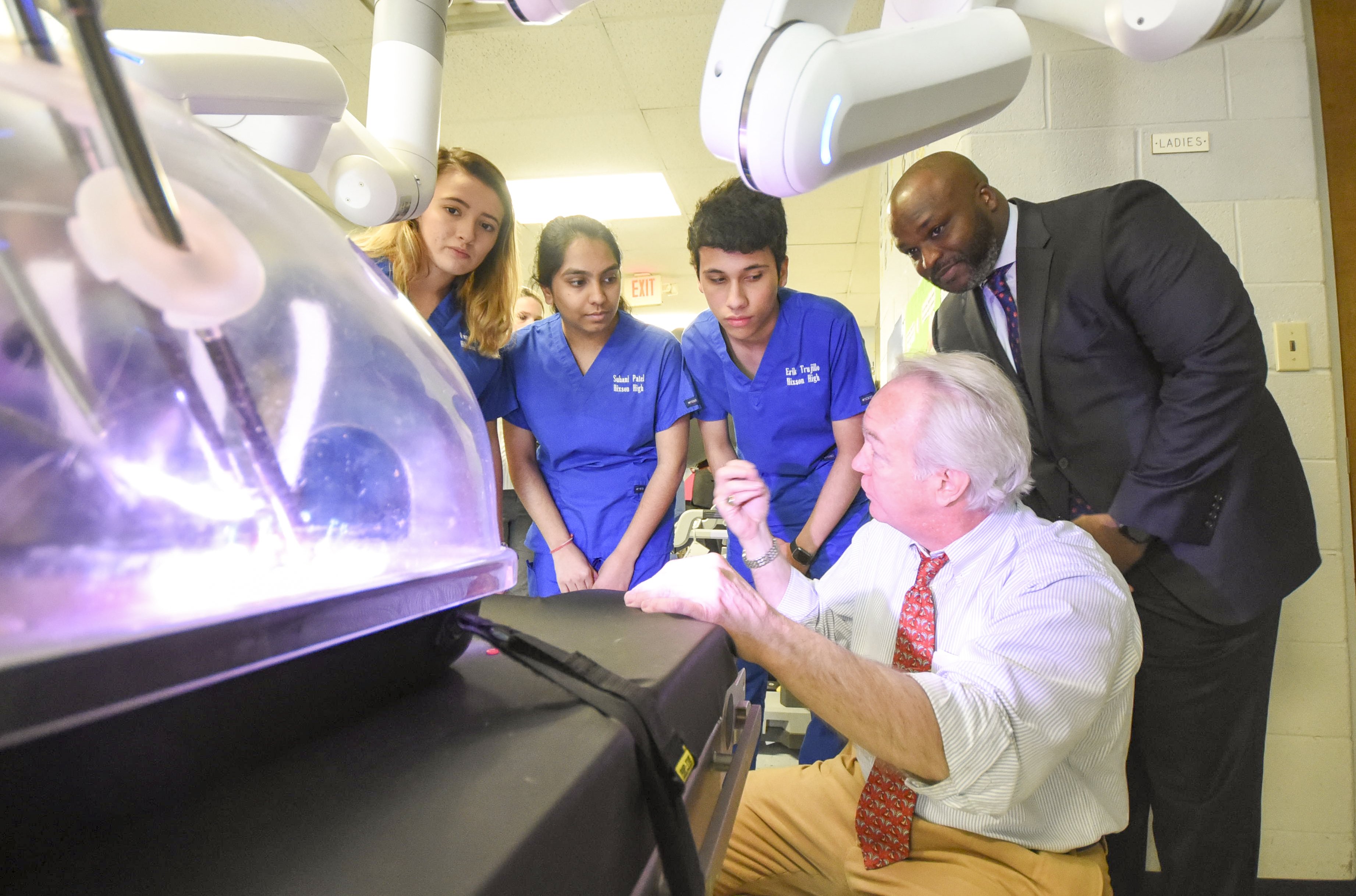 Staff photo by Tim Barber/ CHI Memorial Director of Surgical Services Dr. Lee Jackson, lower right, explains the da Vinci robotics to Hixson High CNA student's Vanessa Blue, left, Suhani Patel and Erik Trujillo Tuesday, Jan. 21, 2020, during the Future Ready Institute partnership in the healthcare instruction area at the school. Hamilton County Schools Superintendant Bryan Johnson listens, top right.