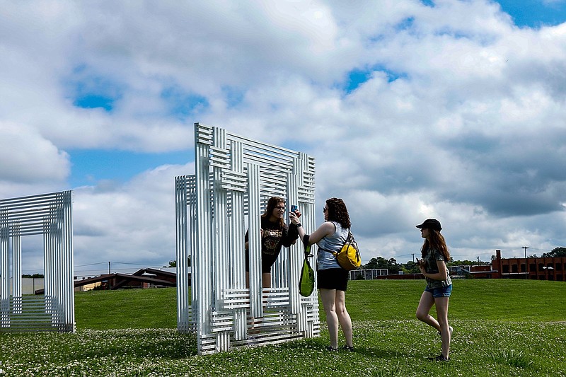 Staff file photo by Troy Stolt / Miranda Knittel of St. Louis, looks at a photo Cara Pelikan made of her with a sculpture as her sister Jessica watches while visiting the Sculpture Fields at Montague Park in June.