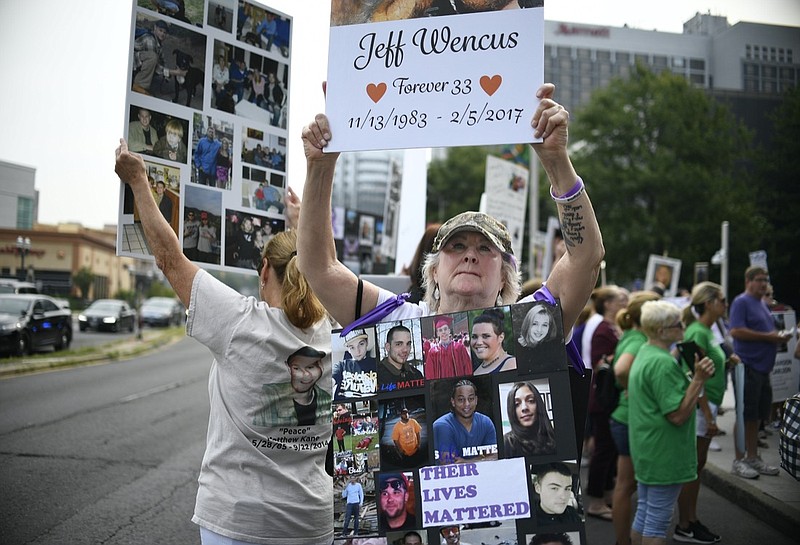 FILE - In this Aug. 17, 2018, file photo, Lynn Wencus of Wrentham, Mass., holds a sign with a picture of her son Jeff and wears a sign of others' loved ones lost to OxyContin and other opioids during a protest at Purdue Pharma LLP headquarters in Stamford, Conn. A landmark settlement in the nation's opioid epidemic is forcing the owners of OxyContin maker Purdue Pharma to give up the company and pay out $4.5 billion. "Am I happy they don't have to admit guilt and give up all their money? Of course not," said Wencus. "But what would that do? It doesn't bring my son back and it doesn't help those who are suffering." (AP Photo/Jessica Hill, File)

